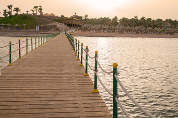 Naklejka premium A large wooden pier is on the sandy beach of the resort. Beautiful view of the tropical coast with a long pantone. Landscape of the sea coast