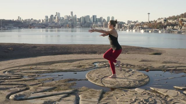 Woman Does an Early Morning Garudasana or Eagle Yoga Pose Standing Balancing Asana As Drone Arc Shot Moves Around Her