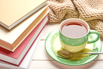Still life on white wooden table top. Green cup of tea, spoon and stack of books in hard cover. Space for your text.