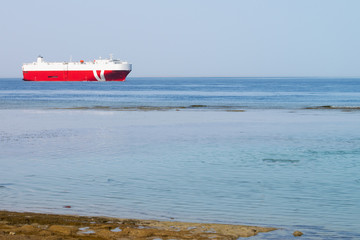 A large cargo ship swims near the shore. Transportation of goods across the sea. A merchant ship is sailing near the beach.