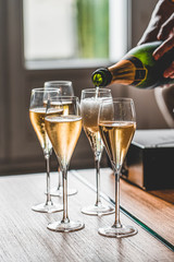 Hand pouring a bottle of champagne into four glasses