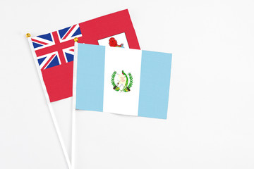 Guatemala and Bermuda stick flags on white background. High quality fabric, miniature national flag. Peaceful global concept.White floor for copy space.