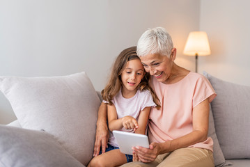 Portrait of grandmother reading stories to cute little girl using digital tablet together, copy...