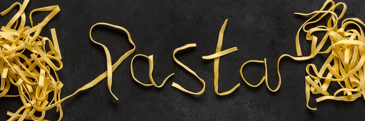 Pasta on black background. Word Pasta made of Tagliatelle. Top view