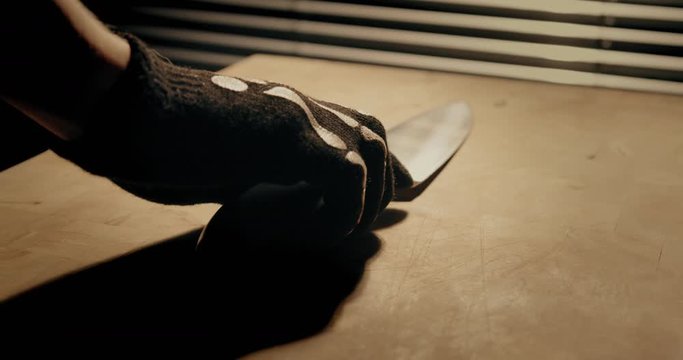 Person with black skeleton halloween gloves pulls a clean butcher-knife from a table. Cinematic slowmotion 4k 100fps