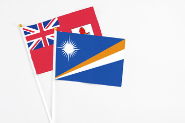 Fototapeta premium Marshall Islands and Bermuda stick flags on white background. High quality fabric, miniature national flag. Peaceful global concept.White floor for copy space.