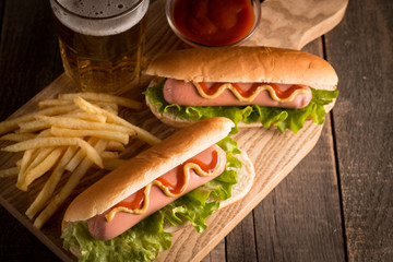 Photo of barbecue grilled hot dog with yellow mustard and ketchup on wooden background. Hot dog sandwich with potato fries and sauces.