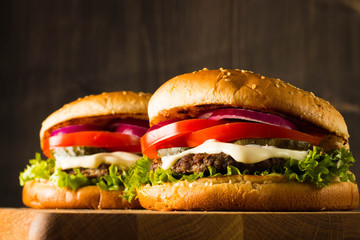 Home made hamburger with beef, onion, tomato, lettuce and cheese. Fresh burger close up on wooden rustic table with potato fries, beer and chips. Cheeseburger.