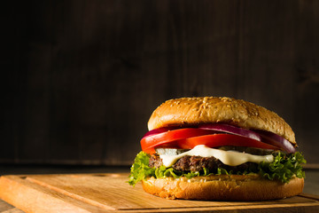 Home made hamburger with beef, onion, tomato, lettuce and cheese. Fresh burger close up on wooden rustic table with potato fries, beer and chips. Cheeseburger.