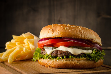 Home made hamburger with beef, onion, tomato, lettuce and cheese. Fresh burger close up on wooden rustic table with potato fries, beer and chips. Cheeseburger.