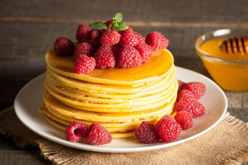 Tasty pancakes with blackberries, banana, raspberries, eggs, honey and maple syrup on wooden background. Morning breakfast concept.