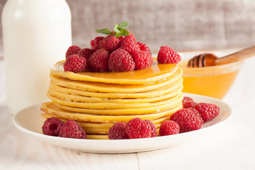 Tasty pancakes with blackberries, banana, raspberries, eggs, honey and maple syrup on wooden background. Morning breakfast concept.