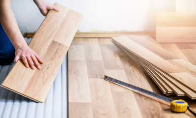 Worker hands installing timber laminate floor. Wooden floors house renovation with measure items.