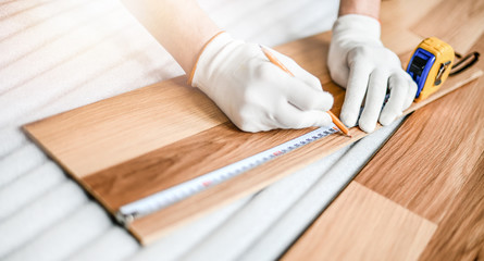 Close up of wood worker with in white gloves measuring tape and new laminated wooden floor board.