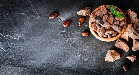 Raw cocoa beans with mint on dark stone table top view, black background. copy space for text....