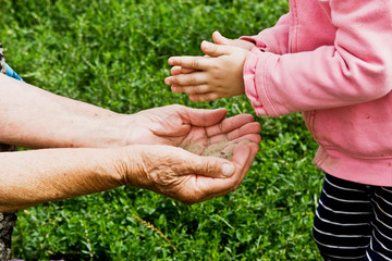 A small child throws sand in the palm of the old grandmother close-up. The pouring sand as a symbol of the fleeting time of our life.