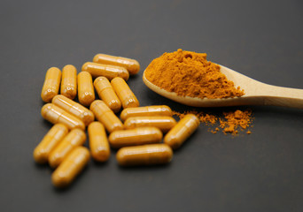 Turmeric powder on the spoon and in the  capsule on black background.