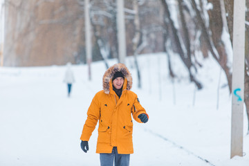 Fototapeta na wymiar man in yellow winter coat with hood walking by snowed park