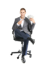 Handsome young businessman with money sitting on chair against white background
