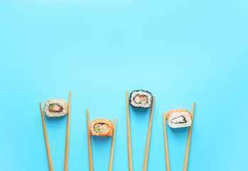 Tasty sushi rolls and chopsticks on color background