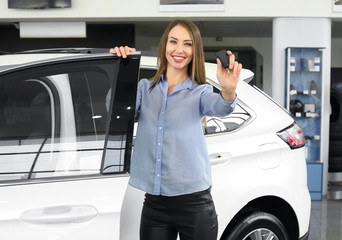 Happy female buyer with key near new car in salon