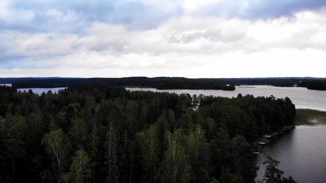 Beautiful drone shot revealing some small cabins in the dark and green scandinavian forest on a cloudy summerday