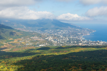 View of Yalta on coast of Black Sea and autumn forest from Ai-Petri mountain on foggy and cloudy sunny day. Crimea, Russia