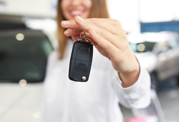 Happy woman with key from new car in salon, closeup
