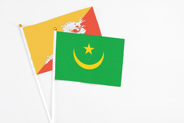 Mauritania and Bhutan stick flags on white background. High quality fabric, miniature national flag. Peaceful global concept.White floor for copy space.