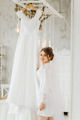 Fototapeta na wymiar The girl in a white coat stands near her wedding dress