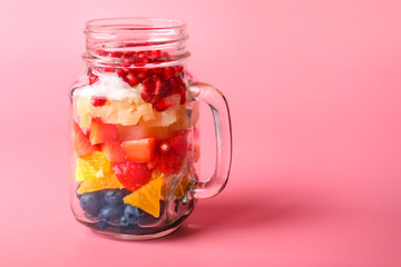 Mason jar with tasty fruit salad on color background