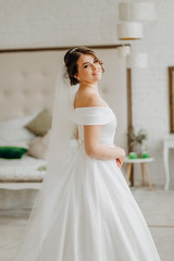 Fototapeta na wymiar Amazing bride in a white dress stands in a room by the bed