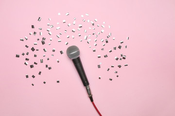 Modern microphone and confetti on color background