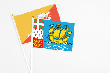 Saint Pierre And Miquelon and Bhutan stick flags on white background. High quality fabric, miniature national flag. Peaceful global concept.White floor for copy space.