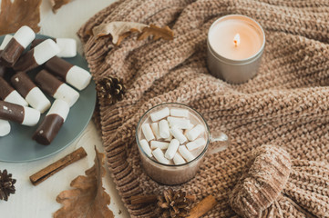 Fototapeta na wymiar Hot drink in winter or autumn with cocoa, chocolate and marshmallows in a cup on a background with a knitted warm sweater and scented candles, top view.