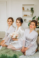 Cute bride with bridesmaids in bathrobes sitting on bed