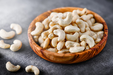 Cashew nuts in a wooden bowl on dark stone board with blurred background.