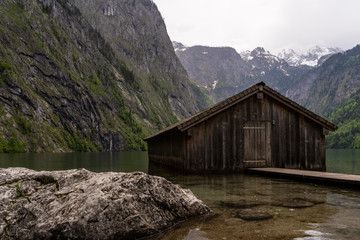 Fototapeta na wymiar Bergsee mit Fischerhütte aus Holz an einem regnerischen wolkigen Sommertag