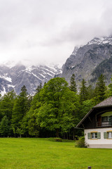 Fototapeta na wymiar Bayrische Berghütte vor einem Wald in den Bergen an einem wolkigen Sommertag