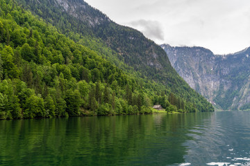Bergsee mit Wald und kleiner Fischerhütte bei wolkigem Wetter