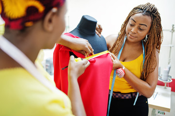 Two african dressmaker woman designed new red dress on mannequin at tailor office. Black seamstress...