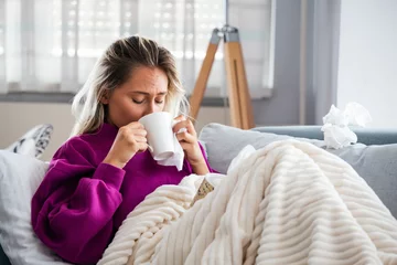 Fotobehang Cold And Flu. Portrait Of Ill Woman Caught Cold, Feeling Sick And Sneezing In Paper Wipe. Closeup Of Beautiful Unhealthy Girl Covered In Blanket Wiping Nose. Healthcare Concept. High Resolution © Graphicroyalty