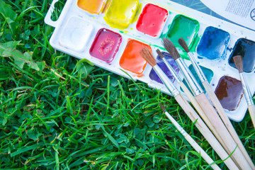 Watercolor paints and tassels of different sizes. Paints and brushes lie on green grass. The heyday of nature. The beginning of a new life. Art.