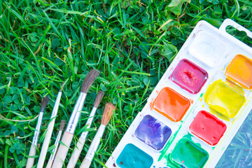 Watercolor paints and tassels of different sizes. Paints and brushes lie on green grass. The heyday...