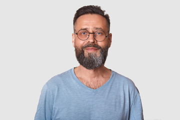 Obraz premium Close up portrait of handsome middle aged bearded Caucasian man with smile, male wearing gray casual t shirt, posing isolated over white background, looking directly at camera, looks satisfied.