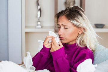 Sick Woman.Flu.Woman Caught Cold. Sneezing into Tissue. Headache. Virus .Medicines. Young Woman Infected With Cold Blowing Her Nose In Handkerchief. Sick woman with a headache sitting on a sofa
