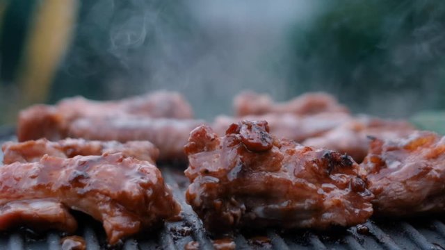 Stock footage HD. Cooked beef steak or pork ribs, toasting meat on a metal electric grill. Royalty high-quality free stock video footage of electric grill stove grilled meat with garden background