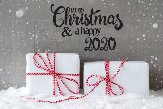Label With English Calligraphy Merry Christmas And A Happy 2020. Two White Gifts With Red Bow. Gray Concrete Background With Snow And Snowflakes