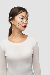 Naklejka premium Medium shot of a young Asian woman in an ivory white blouse and with a stud earring made as a golden bird on the flowers with crystals, jeweller's enamel and a chain with a shimmering pearl.