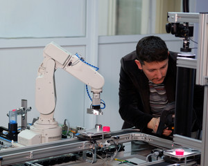 industry 4.0 concept: Man (engineer) is programming robotic arm with control panel (teach pendant) on smart factory production line background. Selective Focus.